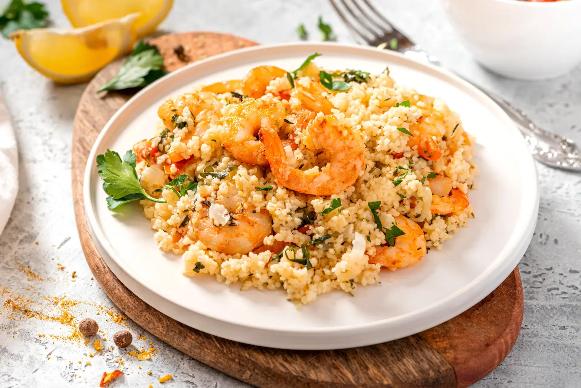 Couscous with shrimps, tomatoes, onions, and herbs in a white bowl close-up