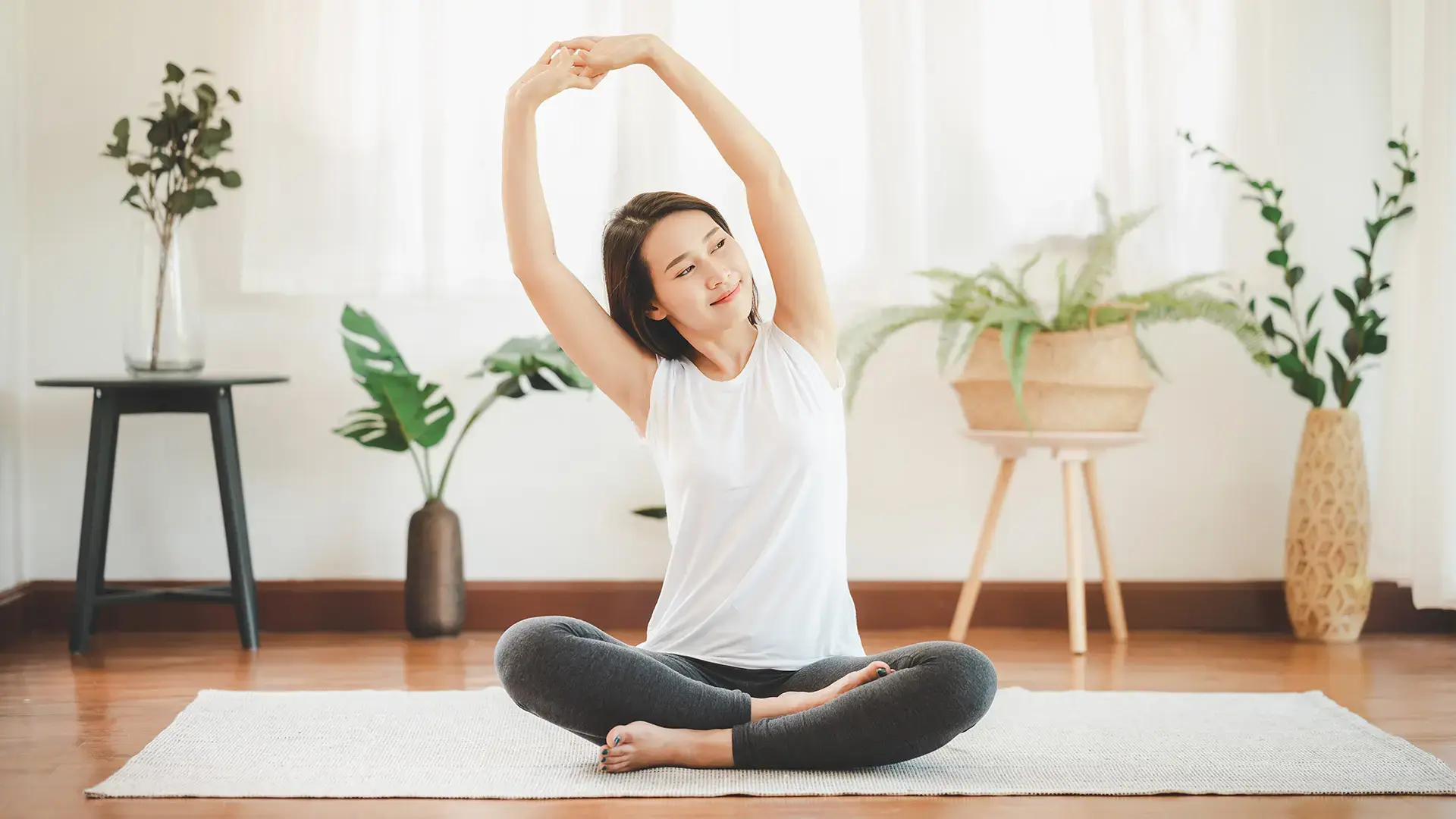 Smiling healthy Asian woman doing yoga shoulder stretching at home in living room