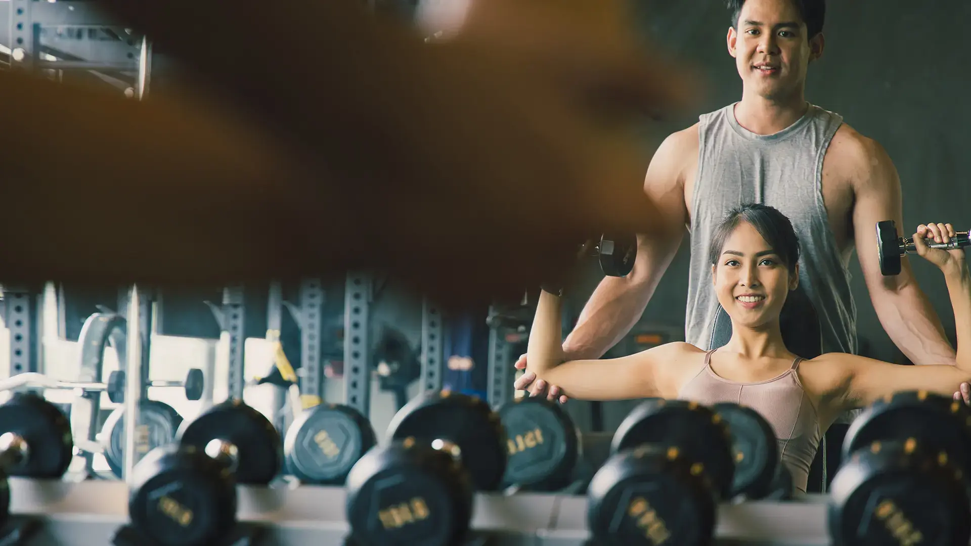 The personal trainer helps Asian women with shoulder workout in gym