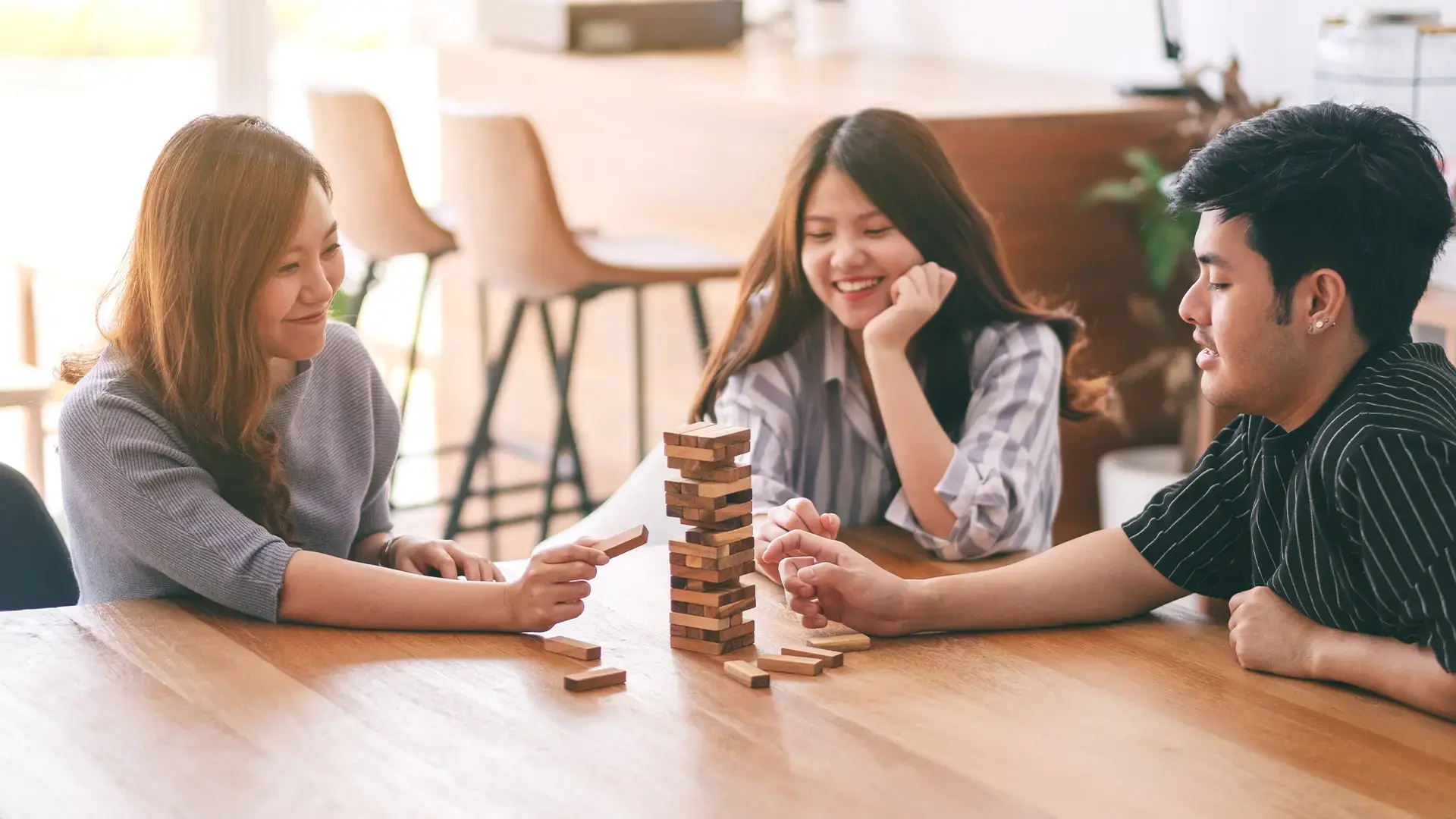 Three-asian-friends-sitting-and-playing-Tumble-tower-wooden-block-game-together-with-feeling-happy
