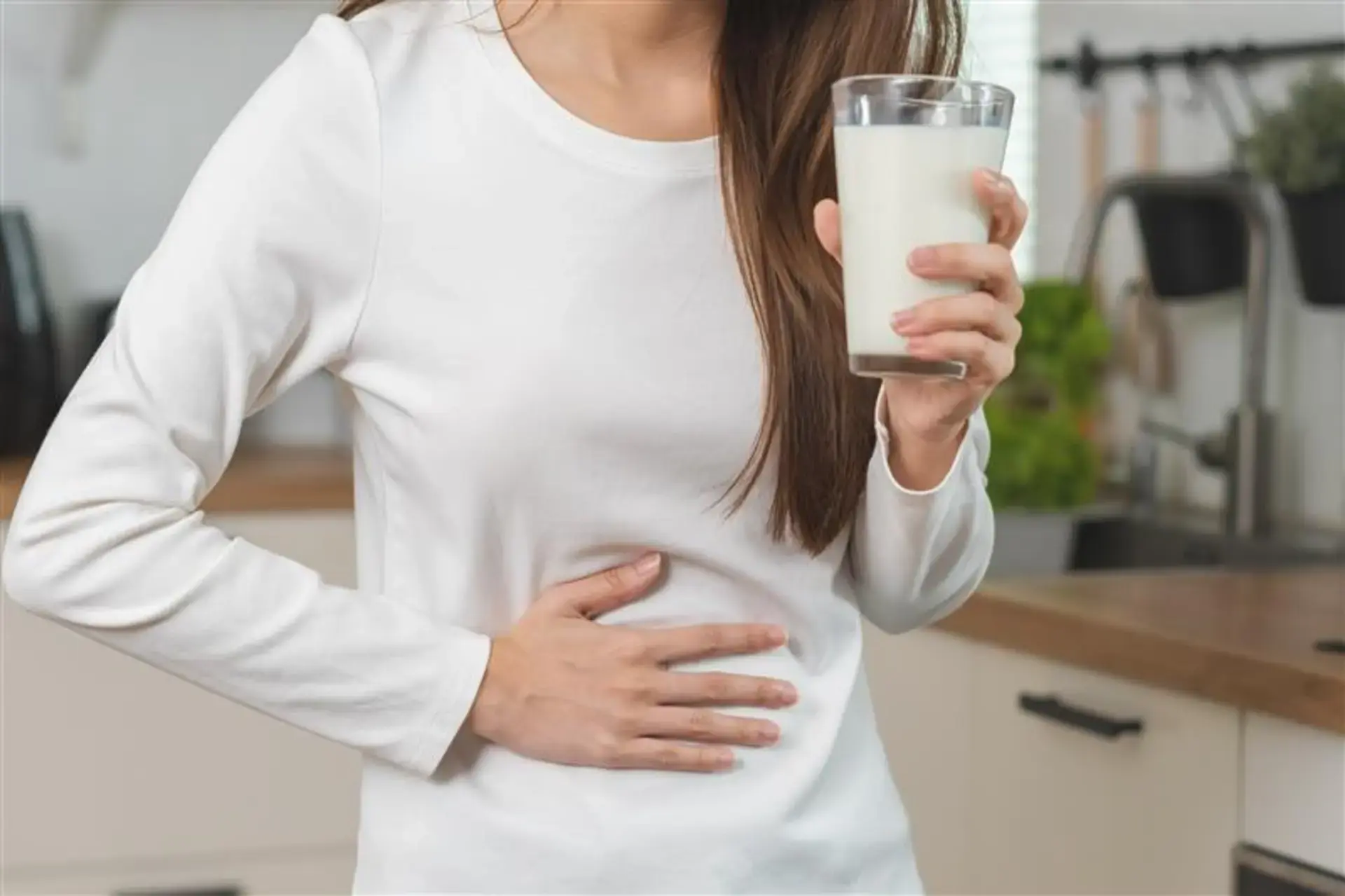 Babae na hawak ang tiyan sa isang kamay, at hawak ang isang basong gatas sa kabilang kamay.