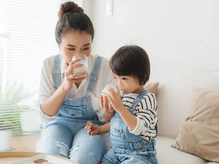 Happy family of asian mom is drinking milk with her cute daughter in the morning at home
