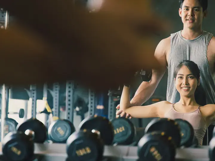 The personal trainer helps Asian women with shoulder workout in gym