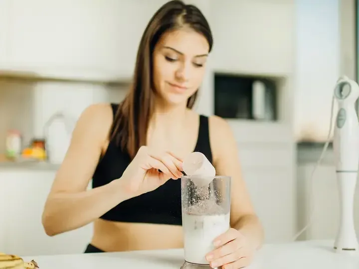 Woman with immersion blender making banana chocolate protein powder milkshake smoothie