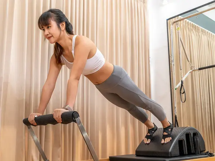 Young Asian woman working on pilates reformer machine during her health exercise