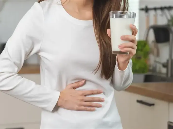 Babae na hawak ang tiyan sa isang kamay, at hawak ang isang basong gatas sa kabilang kamay.