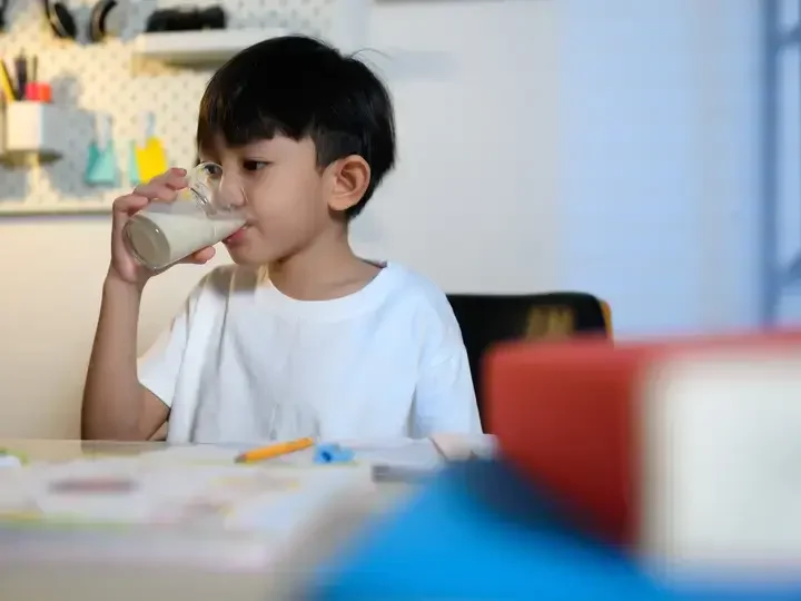 Batang umiinom ng gatas habang nagbabasa ng aklat.